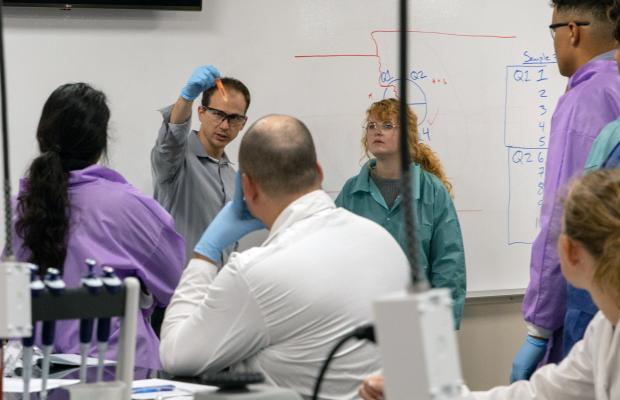 Randy Logan teaching in a lab coat with students watching. 